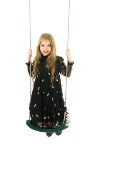 Beautiful little girl swinging in the studio on a swing. Concept of a happy childhood, family well-being.