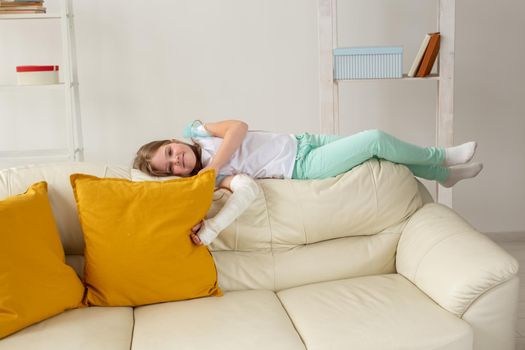 Child with a cast on a broken wrist or arm smiling and having fun on a couch. Positive attitude, recovery and kid.