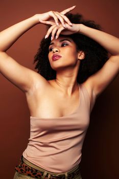 pretty young african american woman with curly hair posing cheerful gesturing on brown background, lifestyle people concept closeup