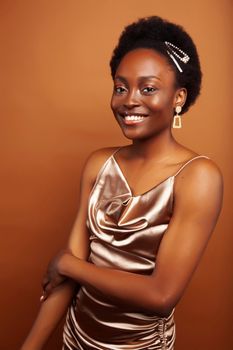 young pretty african model with golden jewelry in fashion style dress smiling happy on brown backround, lifestyle people concept close up