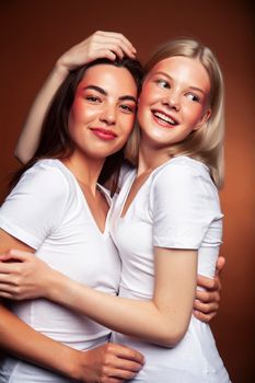 wo pretty diverse girls happy posing together: blond and brunette on brown background, lifestyle people concept close up