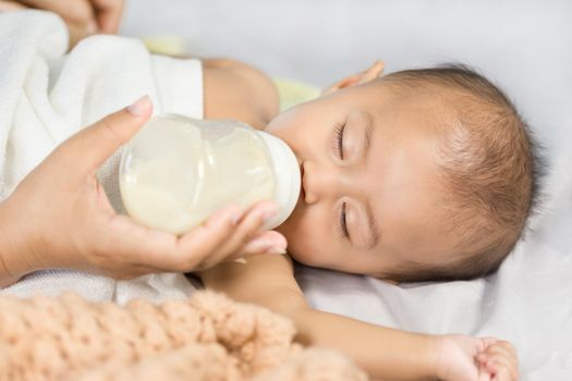 hand of mother feeding milk from bottle and baby sleeping on bed.