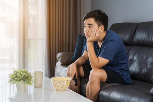 young bored man watching tv and sitting on sofa in the living room