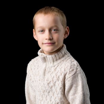 Close up portrait of a cute teenager. Handsome stylish boy in gray knitted jumper looking at camera. Teenage child posing in studio on black background