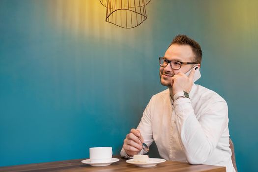 Adult european man businessman with glasses and white shirt talking on the phone in a cafe on a coffee break.