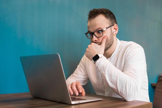 Attractive guy young European businessman works in a laptop sitting at a table in a cafe.