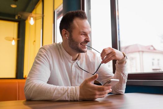 Attractive businessman in a white shirt laughs, holds glasses and sits on the phone.