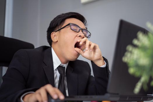 tired young businessman using laptop and yawning 