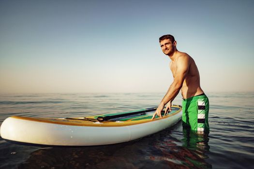 Young fit man on paddle board floating on lake at sunrise