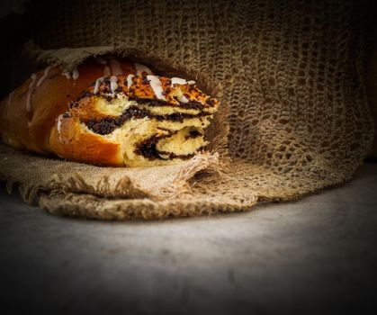 Fresh poppy seed roll on natural linen napkin on rustic wooden background