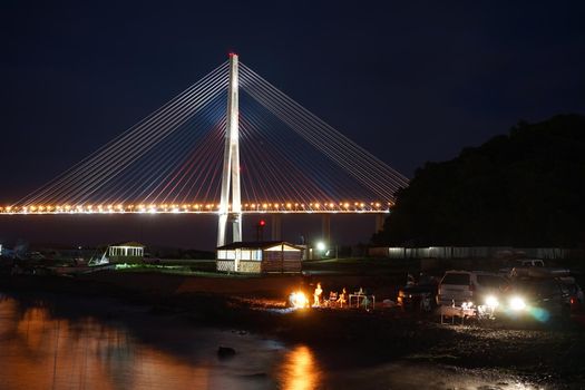 Night landscape with views of the Russian bridge. People relax on the beach. Vladivostok, Russia