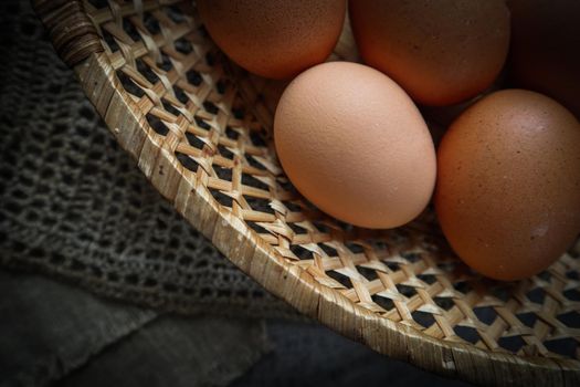 Top view of eggs in a straw basket on a natural linen napkins and a rustic wooden background