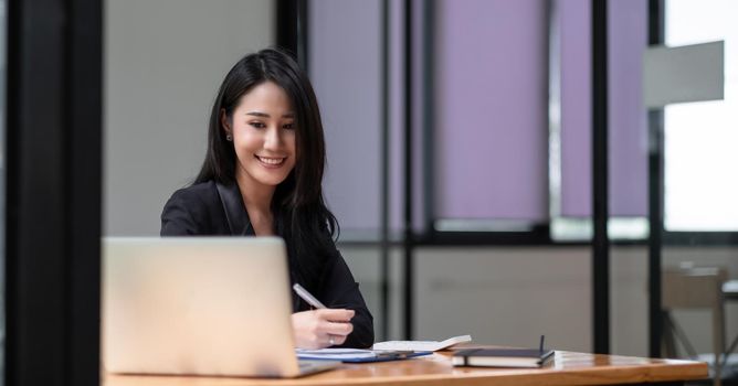 Happy young asian businesswoman sitting on her workplace in the office. Young woman working at laptop in the office.