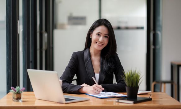 Portrait young asian businesswoman beautiful charming smiling while working with business financial report and laptop in the office.