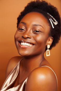 young pretty african model with golden jewelry in fashion style dress smiling happy on brown backround, lifestyle people concept close up