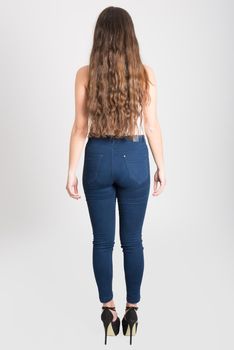 Back view of young woman with long hair wearing white t-shirt and blue jeans on white background