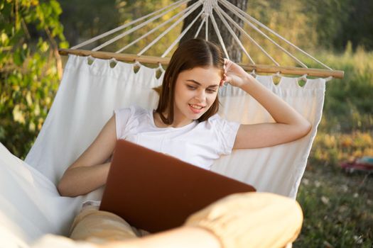 cheerful woman lies in a hammock with a laptop vacation internet travel. High quality photo