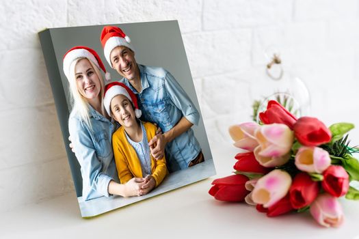 Photo printed on canvas, white background. Happy young family in Santa hats celebrating Christmas at home.