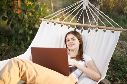 woman outdoors with laptop lies in hammock leisure technology. High quality photo