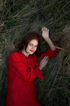 pretty woman in red dress lies on the grass posing top view. High quality photo