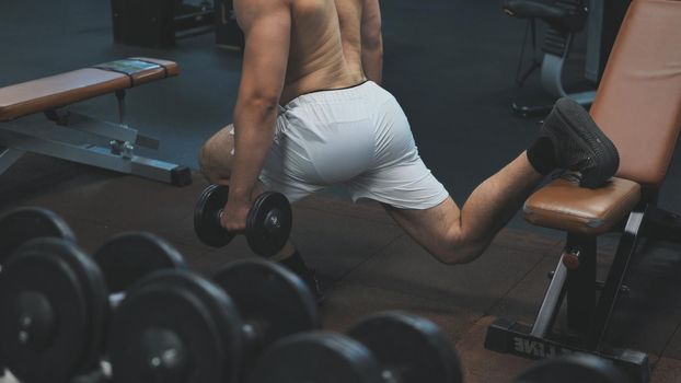 A young man squats with kettlebells for pumping the buttocks