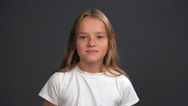 Little disappointed or expecting for more little girl listening parents looking at the camera, wearing white t-shirt and black pants isolated on black background.