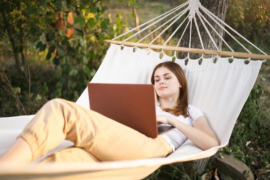 woman outdoors with laptop lies in hammock leisure technology. High quality photo