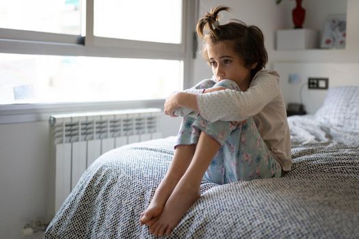 Nine-year-old girl sitting in bed at home bored by confinement