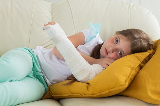 Child with a cast on a broken wrist or arm lying on a couch. Recovery and kid