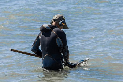 A man with a special device and equipment metal detector looking for lost jewelry and gold in sea water near the beach.