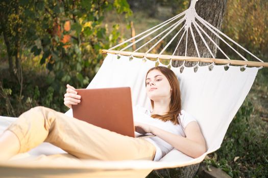 woman outdoors with laptop lies in hammock leisure technology. High quality photo