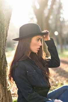 Portrait of thoughtful woman sitting alone outdoors wearing hat. Nice backlit with sunlight
