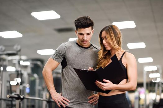 Personal trainer and client looking at his progress at the gym. Athletic man and woman wearing sportswear.