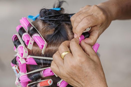 hand of a hairstylist doing a perm rolling the hair of senior woman