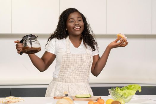 Smiling African Lady has black coffee and a Donut for a snack. Coffee and Sweets for Breakfast. Close-up. High quality photo