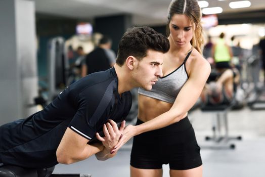 Female personal trainer helping a young man lift weights while working out in a gym