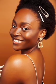 young pretty african model with golden jewelry in fashion style dress smiling happy on brown backround, lifestyle people concept close up
