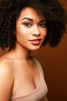 pretty young african american woman with curly hair posing cheerful gesturing on brown background, lifestyle people concept closeup