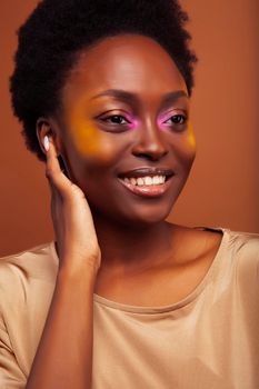 pretty young african american woman with curly hair posing cheerful gesturing on brown background, lifestyle people concept close up