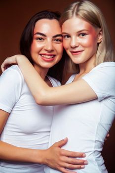 two pretty diverse girls happy posing together: blond and brunette on brown background, lifestyle people concept closeup