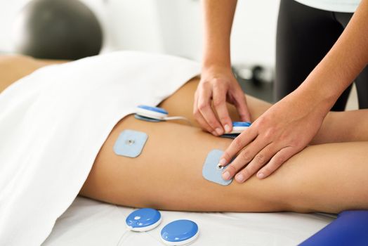 Physiotherapist applying electro stimulation in physical therapy to a young woman. Medical check at the leg in a physiotherapy center.