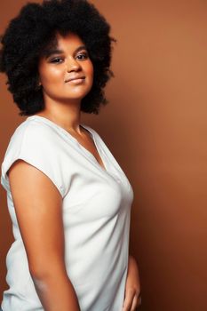pretty young african american woman with curly hair posing cheerful gesturing on brown background, lifestyle people concept close up