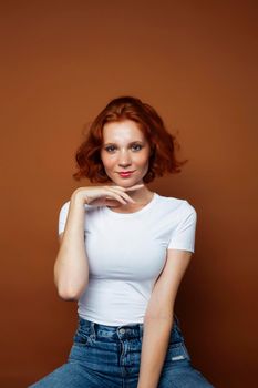 young pretty redhead girl posing cheerful on warm brown background, lifestyle people concept close up