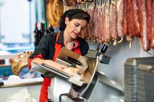 Female butcher cutting york ham in a cutting machine inside a butcher shop.