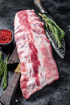 Raw lamb loin spare ribs on a cutting board with knife. Black background. Top view.