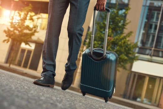 Businessman is travelling. Cropped photo of a man in suit pulling his luggage while walking outdoors. Business concept. Trip