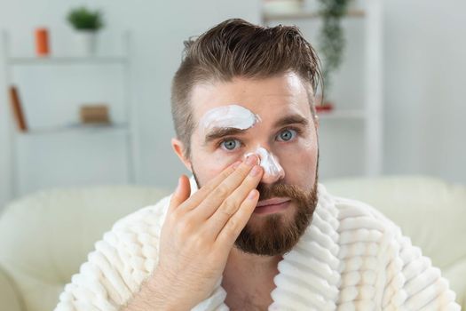 Bearded guy applying anti-wrinkle cream on his face. Skin care and spa for man concept
