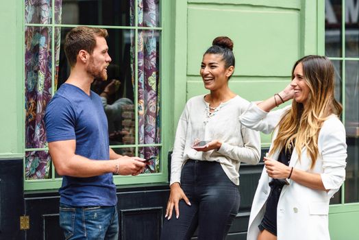 Three multiethnic people laughing outdoors with smart phone in their hands. Multiracial group of friends having fun in urban background.