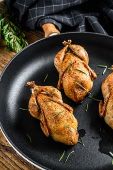 Homemade roast quail in a pan. Wooden background. Top view.