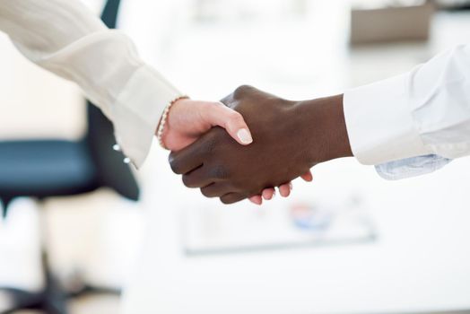 Black businessman shaking hands with a caucasian businesswoman wearing suit in a office. Close-up shot